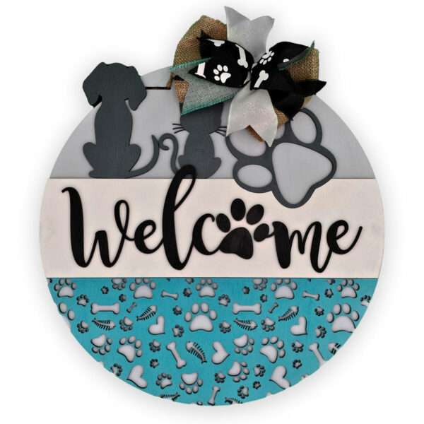 This round decorative sign, named "Welcome Cats and Dogs" by Rustic Road Creations, beautifully captures a pet theme. It displays the word "welcome," cleverly using a paw print as the "o," alongside silhouettes of a dog and cat, and features a large paw print. The bottom section is adorned in teal with a charming pattern of paw prints, bones, and hearts. Completing the design is an elegant bow at the top.