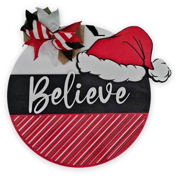 A round Christmas-themed sign features a Santa hat and the phrase "Believe in Santa" in cursive letters. The top portion is white with a decorative bow, while the bottom is red with diagonal stripes. The bottom half is black with the text in white.