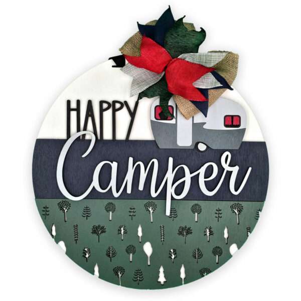 A round decorative sign featuring the text "Happy Camper." The sign has a RV camper, a red and green plaid bow, and a design of trees at the bottom. The background is divided into sections of white, dark blue, and green.