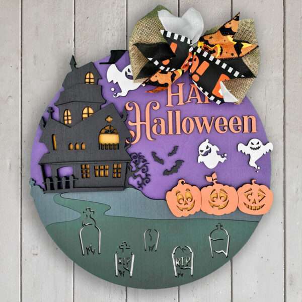 A round wooden Halloween sign features a haunted house, ghosts, bats, pumpkins, and tombstones set against a purple and green backdrop. Adorned with a large bow of Halloween-themed ribbons at the top, it joyfully proclaims "Happy Halloween" in vibrant orange letters.