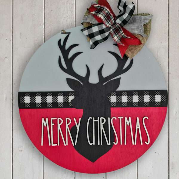 A round custom door sign featuring a black silhouette of a reindeer's head with antlers, set against a red and gray background with a black-and-white plaid stripe. The text "MERRY CHRISTMAS" is in white, and a red, black, and white plaid bow adorns the top. Perfect for your merry christmas deer décor! The sign is placed on a white wood background.