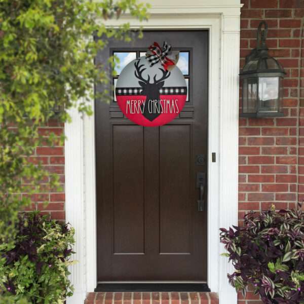 A round custom door sign featuring a black silhouette of a reindeer's head with antlers, set against a red and gray background with a black-and-white plaid stripe. The text "MERRY CHRISTMAS" is in white, and a red, black, and white plaid bow adorns the top. Perfect for your merry christmas deer décor! The sign is showcased on the front door of a home.