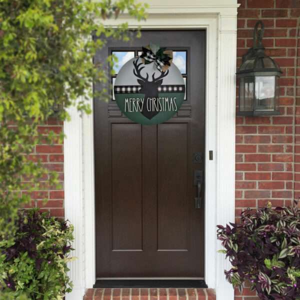 A round Christmas decoration featuring a black silhouette of a merry Christmas deer in the center. "Merry Christmas" is written below the reindeer. The top boasts a plaid and burlap bow with green leaves, while a black and white plaid strip adorns the middle, making it an ideal custom door sign. The sign is showcased on the front door of a home.