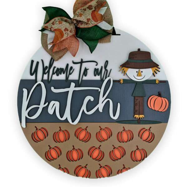 A round autumn-themed custom door sign with a decorative bow at the top. The sign reads "Welcome to our Patch" and features a scarecrow holding a pumpkin. The bottom half of the sign is decorated with multiple small pumpkins.