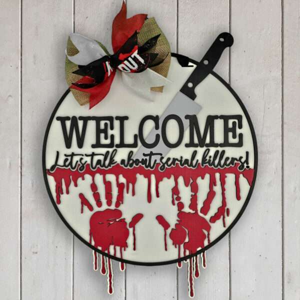 Round sign with a butcher knife and a bow at the top. "WELCOME" is printed boldly, followed by "Let's talk about serial killers!" Red blood-like handprints and drips decorate the lower half. The sign hangs on a white wood background, perfect for adding a touch of Halloween eeriness.