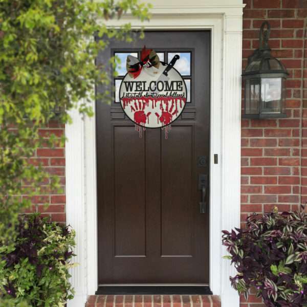 A front door with a dark brown finish has a Halloween-themed wreath hanging on it, featuring bloodstains, white handprints, and the word "WELCOME" with the phrase "Enter if you dare" below. A custom door sign reads, "Welcome! Let's talk about serial killers," framed by brick walls and plants on either side.