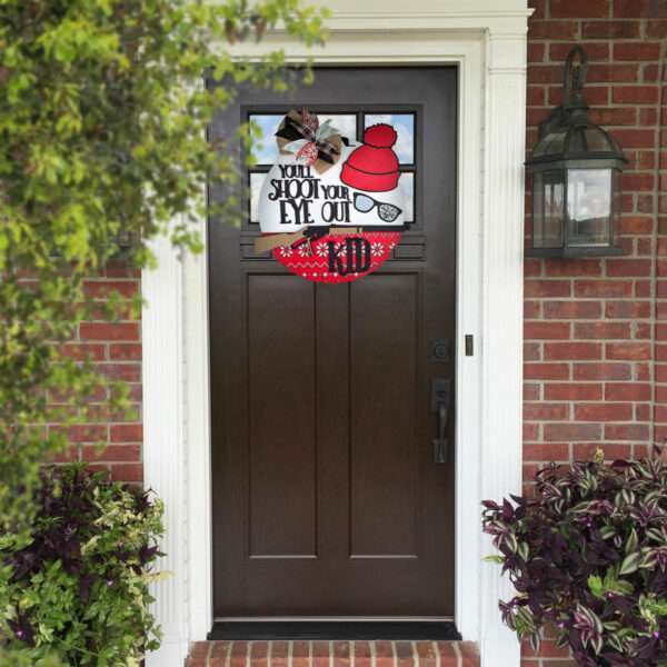 A front door with a custom door sign featuring a red hat and the words "You'll Shoot Your Eye Out" above a pair of broken glasses. The door is surrounded by red brick walls, white trim, and potted plants on either side. A lantern-style light fixture is on the right.