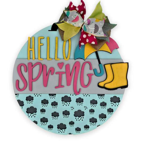 A round sign with the text "HELLO SPRING" in bold yellow and pink letters. An umbrella, rain boots, and a multicolored bow decorate the sign. The bottom section features a pattern of dark clouds and raindrops on a light blue background, perfectly capturing the essence of spring showers.