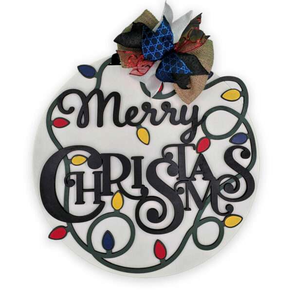 A circular Christmas decoration with the words "Merry Christmas" in black, ornate font. The decoration is adorned with a string of colorful Christmas lights and topped with a festive bow made of various fabrics.