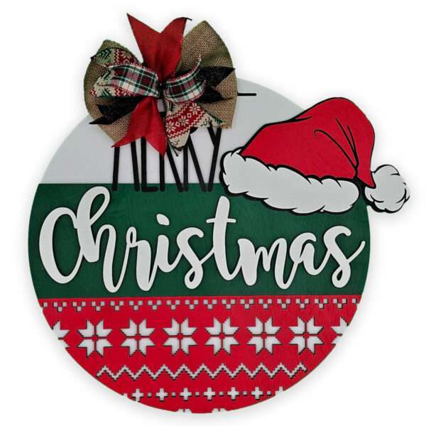 A festive circular Christmas sign features a large "Merry Christmas" message, accented with a Santa hat on the top right. The top is decorated with a bow made of red, black, and plaid ribbons. The bottom has a red and white snowflake pattern.