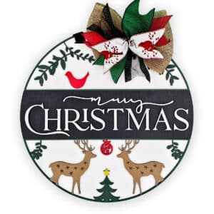 A round, custom wood door sign featuring the text "Merry Christmas" in the center. The sign is decorated with green leaves, a red bird, two merry Christmas deer with snowflake patterns, a Christmas tree with a star on top, and a red, green, and burlap bow at the top.