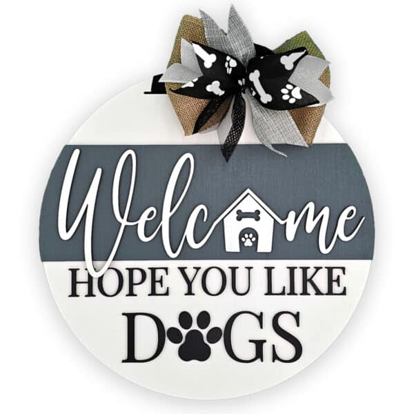 This charming round wooden door sign warmly greets visitors with the text, "Welcome Hope You Like Dogs." It showcases a small doghouse and playful paw prints, beautifully embellished with a burlap bow adorned with paw print ribbons.