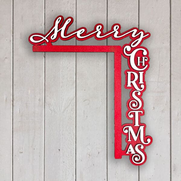 A festive sign with "Merry Christmas" in red and white lettering, arranged in an L-shape. "Merry" is written horizontally and "Christmas" is vertically aligned. The sign is mounted on a light wooden wall.